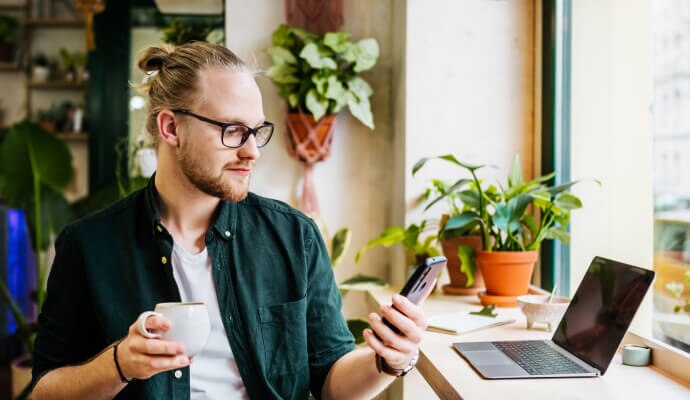 Homme buvant une tasse de café avec un téléphone portable protégé par Norton 360 for Mobile.